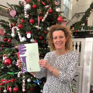 teacher holding up certificate in front of a christmas tree