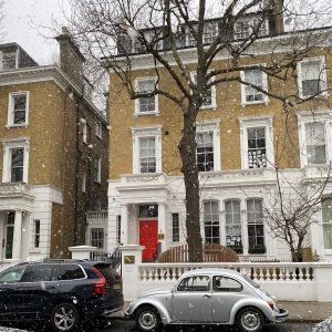 A shot of a house with cars parked outside, and it is snowing.
