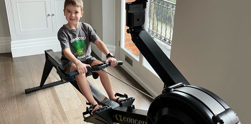 A young boy in their living room at home sat on a rowing machine.